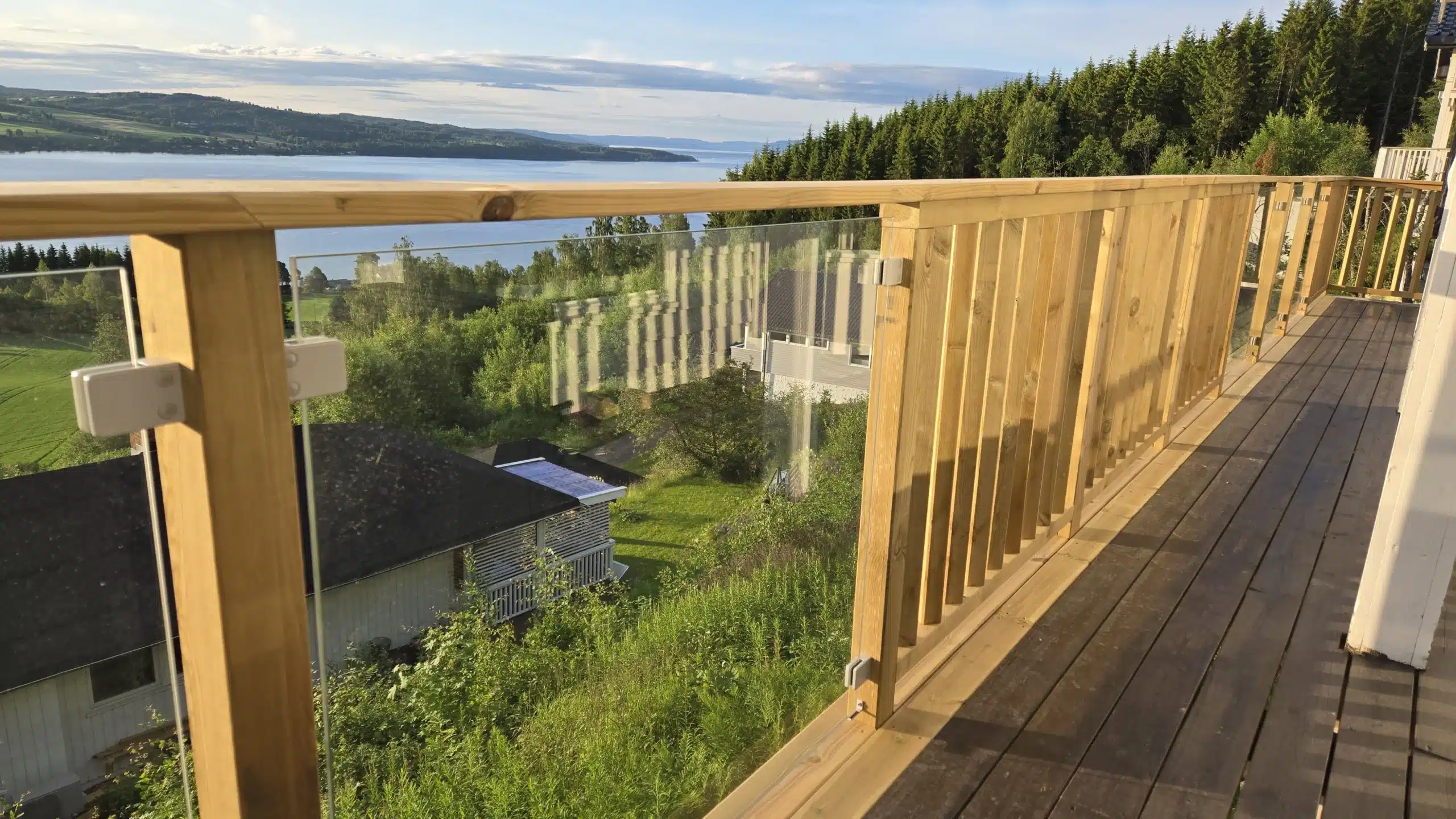 Altanräcke med glas och träöverliggare med utsikt över skog och vatten.