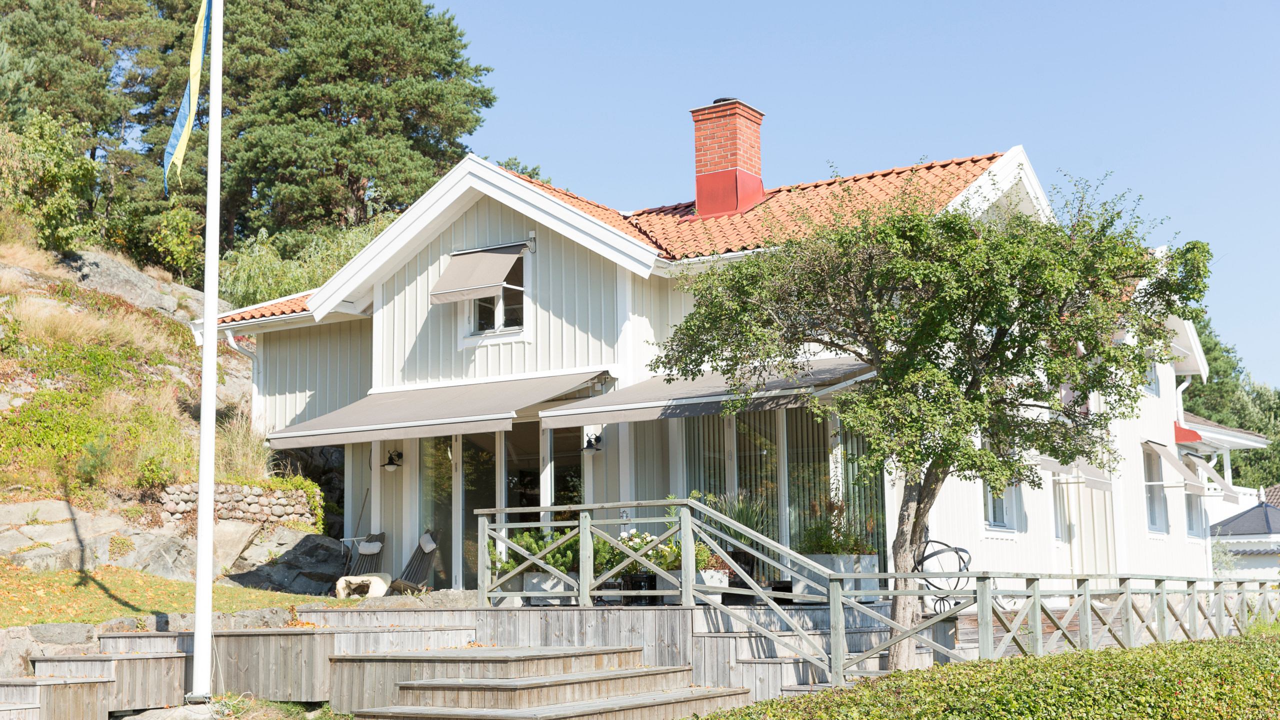 Terrassmarkis monterad på fasad över altan med matgrupp i skugga.