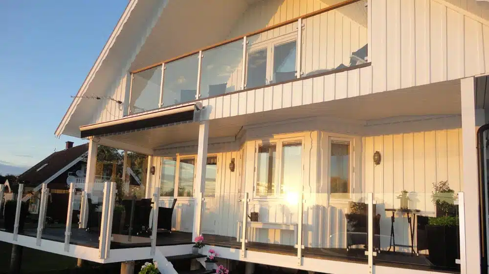 Lång balkong med glasräcke på trähus i kvällssol