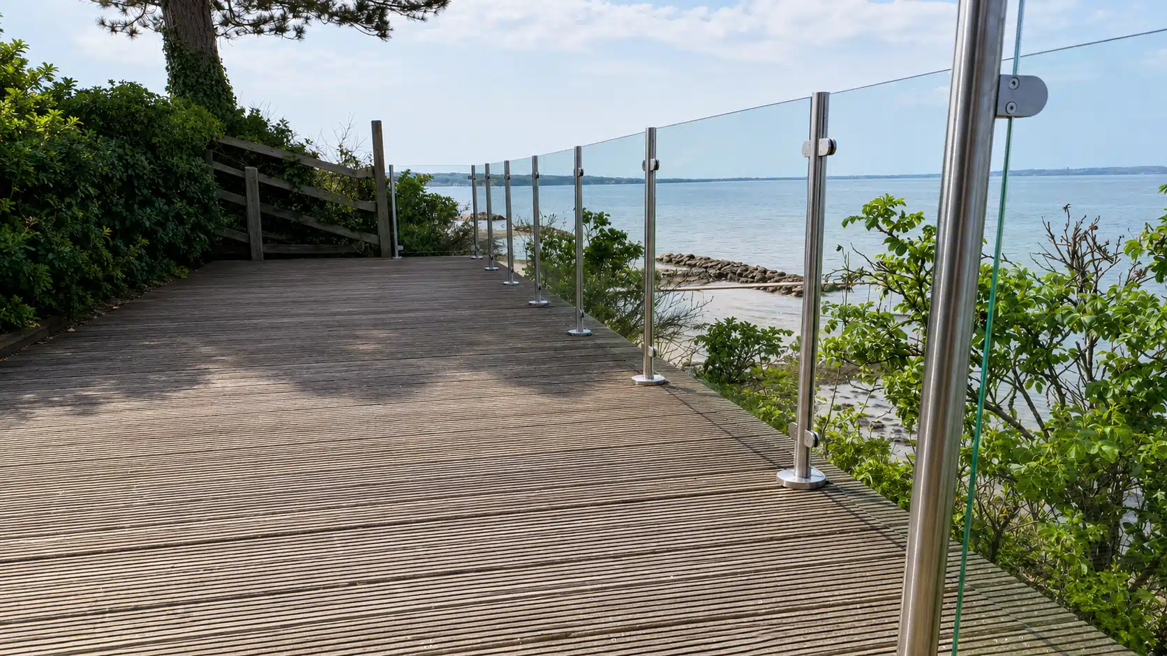 Glasräcke med rostfria stolpar på terrass med fri sikt mot havet.