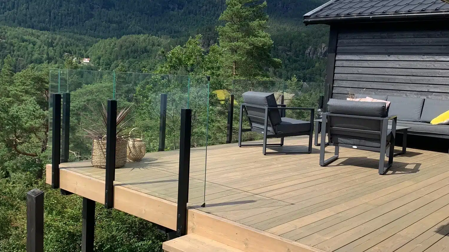 Glasräcke med svarta stolpar på en altan med utsikt mot berg.