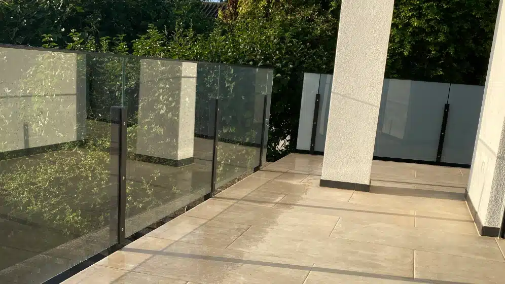 Glasräcke med tonat säkerhetsglas på en terrass vid en vit fasad.