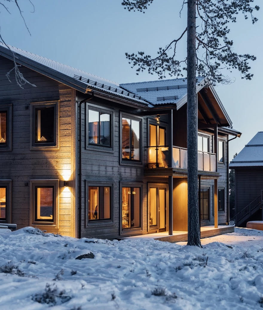 Modernt trähus i snötäckt vintermiljö med glasräcke på balkongen.