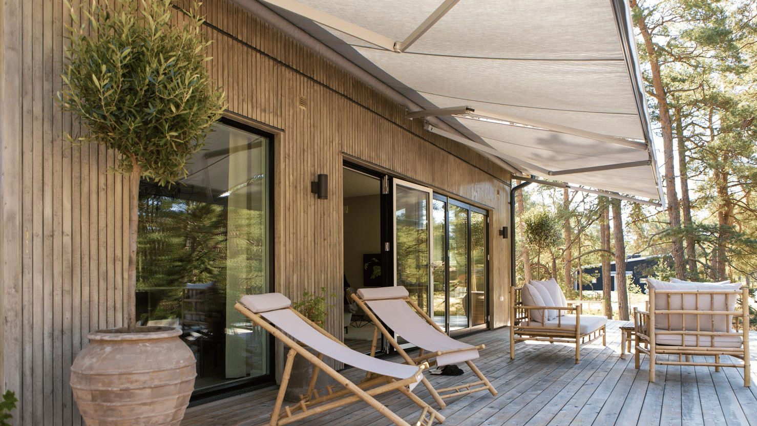 Stor terrassmarkis utfälld över trädäck med loungestolar och uteplats.